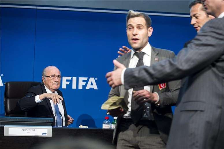 El presidente de la FIFA, Joseph Blatter (i), junto al humorista británico Simon Brodkin (c), quien le lanzó una lluvia de billetes durante una rueda de prensa para presentar los resultados de la reunión del Comité Ejecutivo de la FIFA en su sede de Zúrich, Suiza. EFE