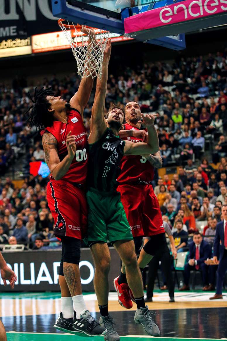El pivot argentino del Joventut Marcos Delía (c) entra a canasta ante los jugadores del Tecnyconta Zaragoza Stan Okoye (d) y Javier Justiz durante el partido de Liga Endesa que se disputó en el Municipal de Badalona.EFE