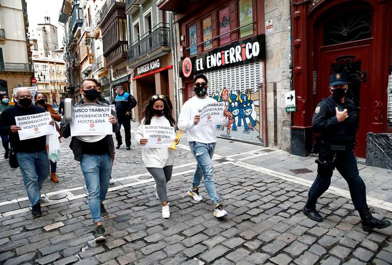 Un efectivo de la Policía Nacional acompaña a un grupo de trabajadores del sector de la hostelería que se han concentrado este miércoles en el recorrido por donde han pasado los ciclistas en la salida neutralizada que ha tenido lugar en el barrio de la Rochapea en la segunda etapa de la Vuelta Ciclista a España que ha salido de Pamplona y finaliza en la localidad navarra de Lekumberri. EFE/ Jesús Diges