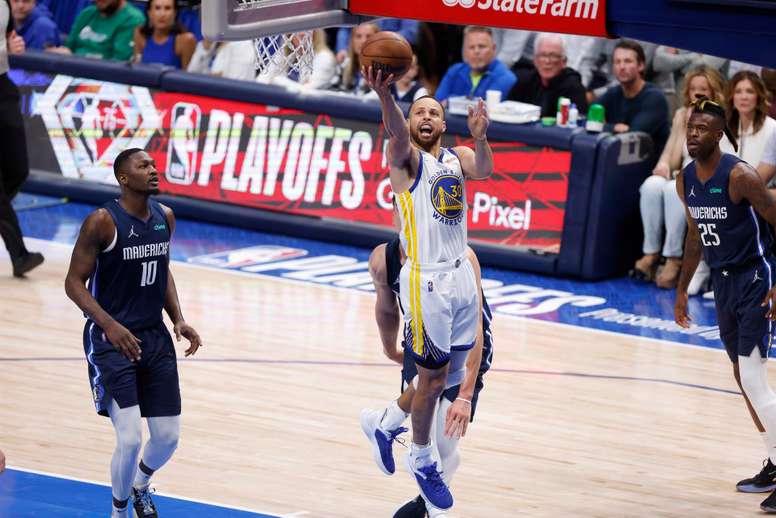 El escolta de los Golden State Warriors, Stephen Curry (c), hace una bandeja para vencer al escolta de los Dallas Mavericks, Luka Doncic (centro, atrás). EFE/EPA/ADAM DAVIS
